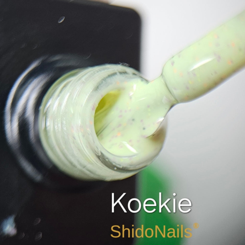 Detailfoto van de ShidoNails gellak kleur Koekie, een pastelgroene lak met subtiele donkere spikkels.